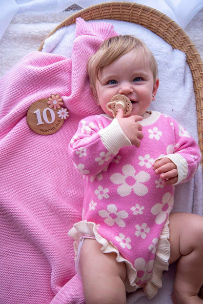 Baby wearing the Little Violet Threads Violet Ruffle Romper in pink floral knit, lying in wicker bassinet beside matching pink blanke