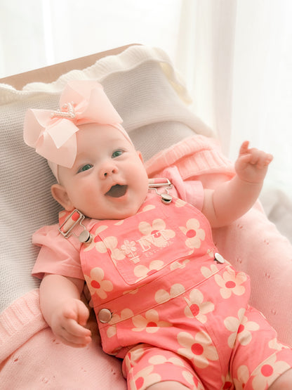 baby wearing little violet threads violet baby overalls with floral print sitting on pink blanket