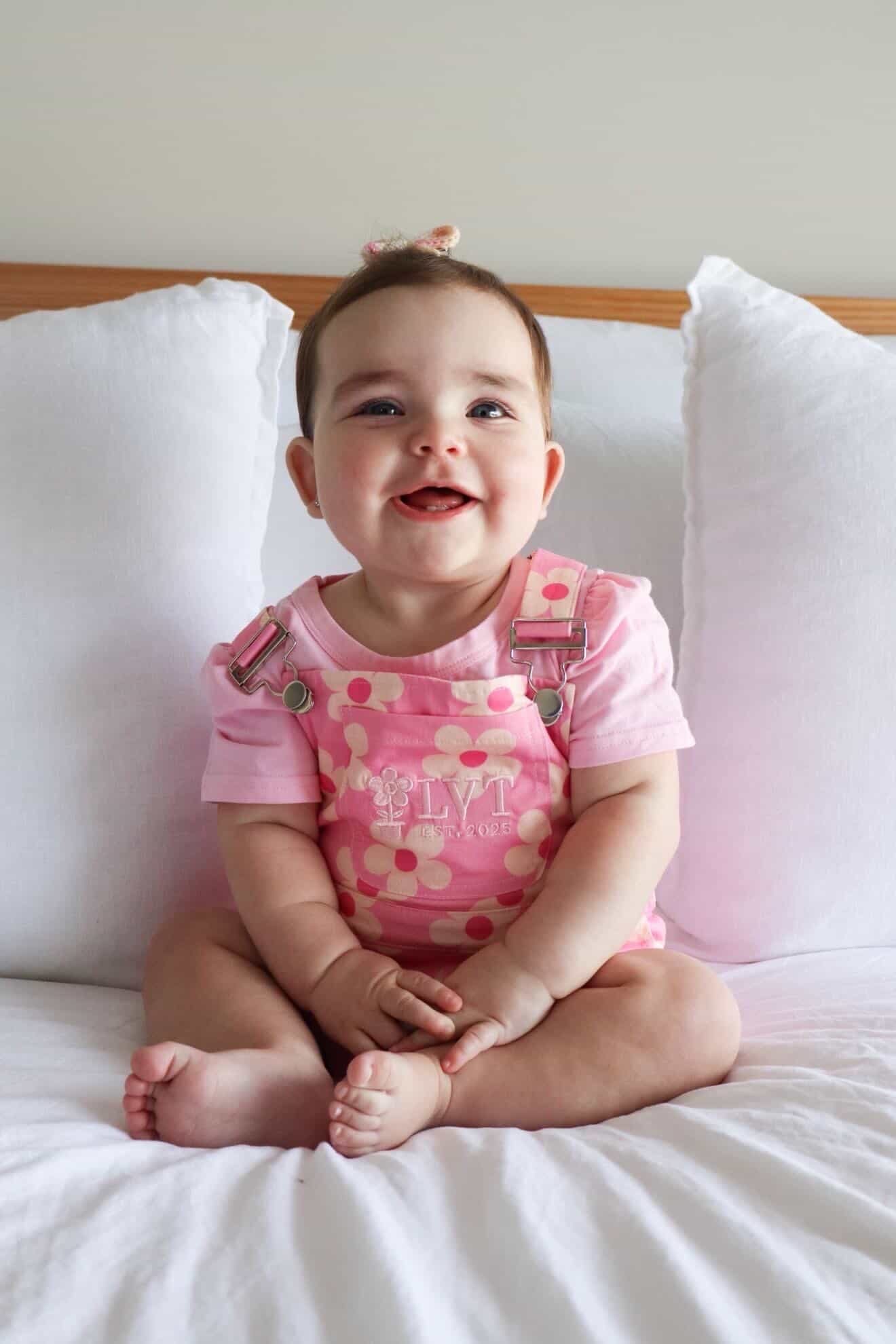 Child wearing pink polka dot overalls sitting on a bed